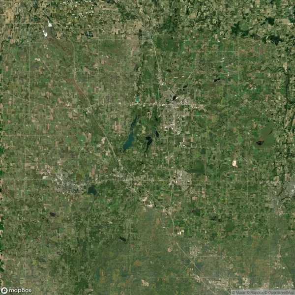 Satellite view of a mostly green landscape with scattered urban areas, roads, and a few water bodies.
