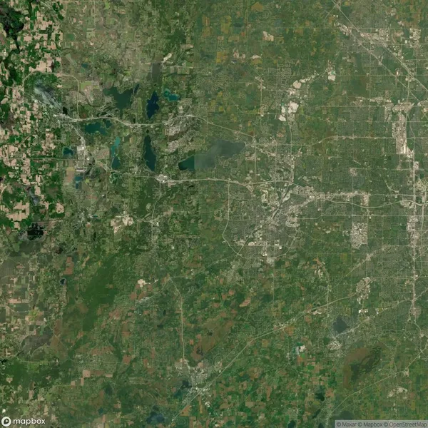 Satellite view of a sprawling urban and rural landscape with patches of greenery, roads, lakes, and various land patterns, depicting a diverse terrain.