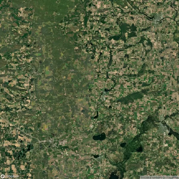 Aerial view of a patchwork landscape with a mix of green forests, agricultural fields, and a few scattered lakes and rivers. Roads are visible traversing the terrain.
