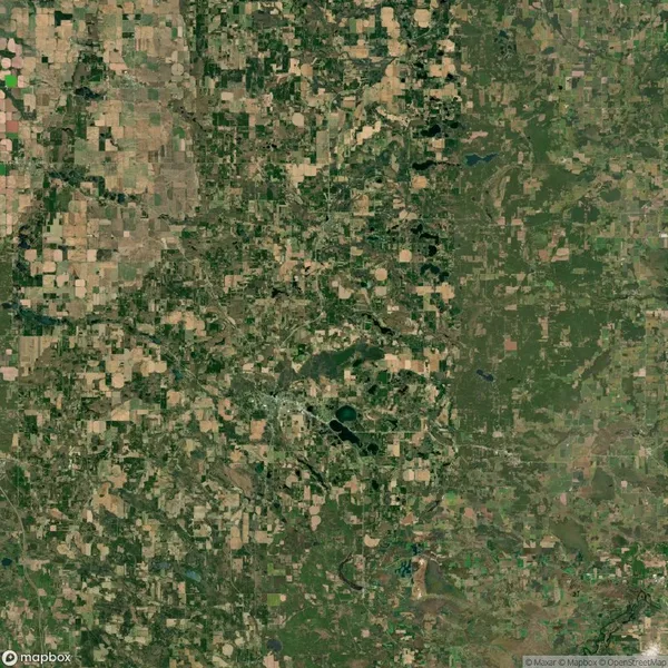 Aerial view of a landscape showing a mix of patchwork farmland and green, wooded areas with a few scattered water bodies.
