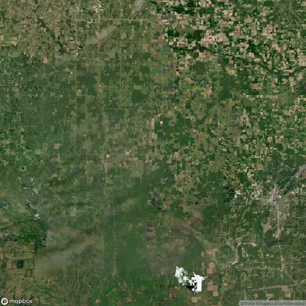 Aerial view of a rural landscape with patchwork fields and scattered greenery across the area. There are clusters of denser vegetation and a few visible roads.