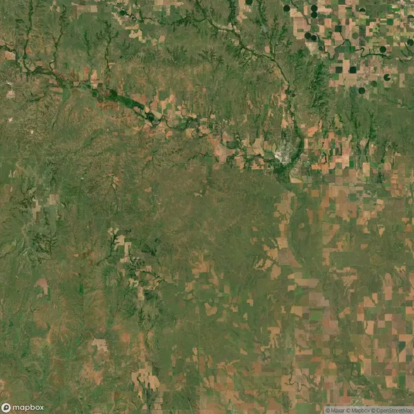 Aerial view of a rural landscape showing a mix of fields, farmland, and patches of trees with a river winding through the upper part of the image.