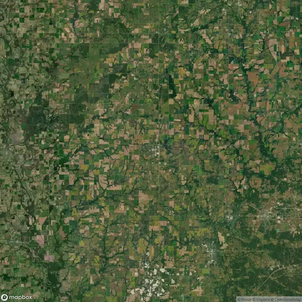 Aerial view of a rural landscape showing a patchwork of farmland, fields, and green areas with scattered waterways and a clustered town in the lower right.