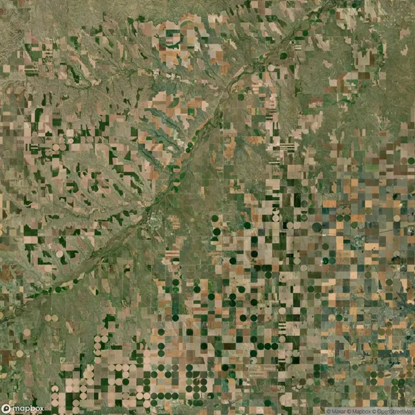 Aerial view of farmland with a patchwork of square and circular fields, intersected by a river and varied shades of green and brown.
