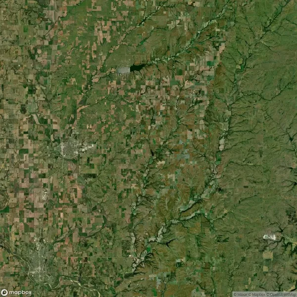 Satellite image showing a landscape with a mix of farmland, small urban areas, and forested river valleys under clear weather conditions.