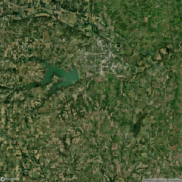 A satellite view shows a patchwork of farmland, a large reservoir, a river, and a small urban area surrounded by green fields and forests.