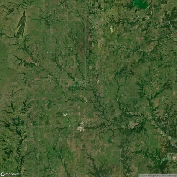 A satellite view of a rural landscape featuring a patchwork of fields, winding rivers, and scattered wooded areas.