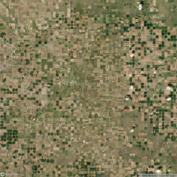 Aerial view of farmland featuring a patchwork of square and circular fields in various shades of green and brown.