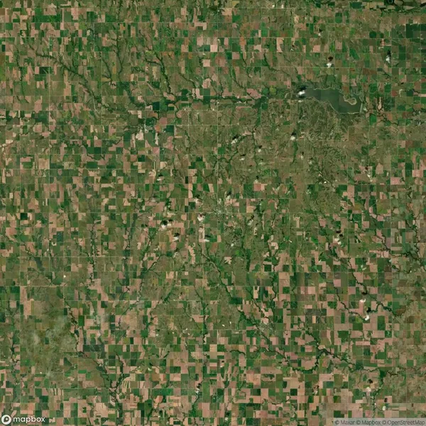 Aerial view of a patchwork landscape with rectangular agricultural fields, intersecting roads, and scattered vegetation in various shades of green and brown.