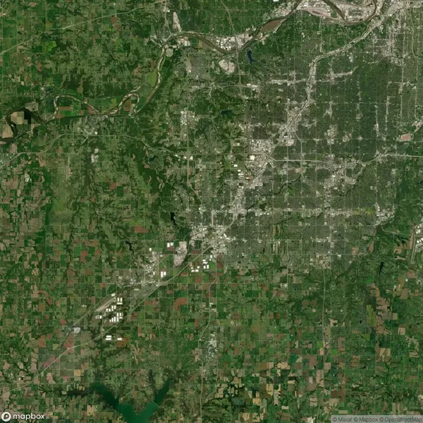 A satellite view shows an urban area with a dense network of roads surrounded by rural and forested regions, farmland, and a few bodies of water.