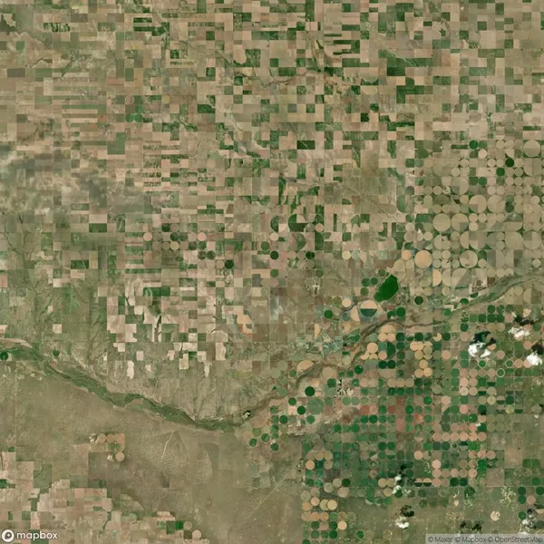 Aerial view of patchwork farmland with a mix of square and circular fields, intersected by a river and patches of green vegetation.