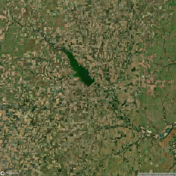 A satellite view of a patchwork landscape with a large lake near the center, surrounded by agricultural fields and intersected by roads and water channels.