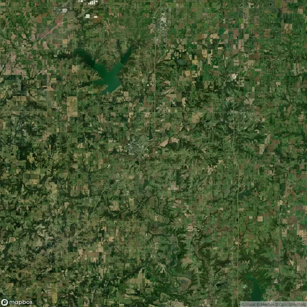 Aerial satellite view of a rural area with patchwork fields, forests, rivers, and a large bird-shaped lake near the top left.