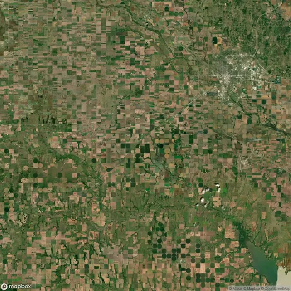 Aerial view of a large area with a patchwork of agricultural fields, a city in the upper right, and a river or reservoir in the lower right corner.