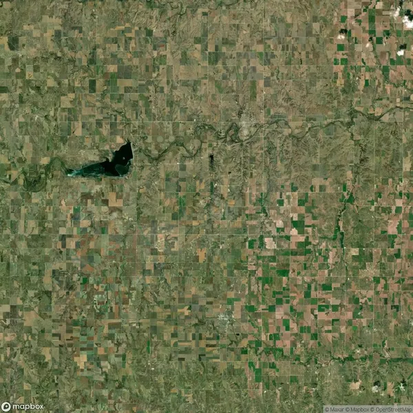 Satellite view of a rural landscape with a patchwork of agricultural fields, a river running horizontally, and a dark irregular-shaped lake on the left side.