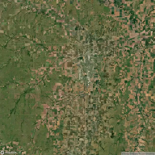 Aerial view of a rural landscape featuring a town at the center, surrounded by green fields and farmland divided into rectangular plots.