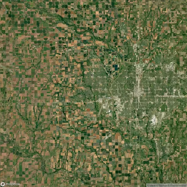 Aerial view of an urban city surrounded by a patchwork of farmland and fields, with roads and rivers visible throughout the landscape.