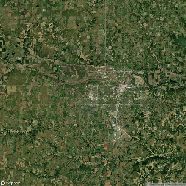 Satellite image showing an aerial view of a city with a river running through it, surrounded by agricultural fields and patches of woodland.
