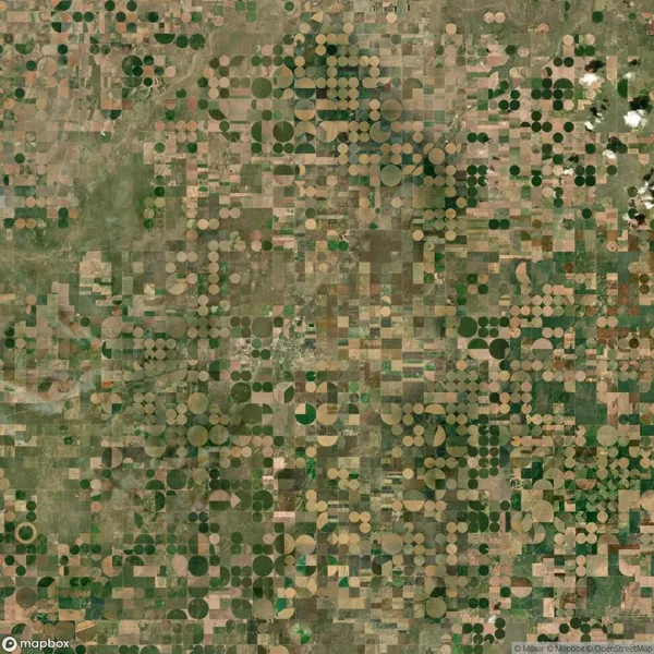 Aerial view of farmland with a grid pattern featuring circular and rectangular agricultural fields in various shades of green and brown.