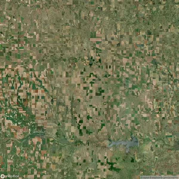Aerial satellite view of a rural landscape with rectangular agricultural fields, patches of greenery, and a small body of water near the bottom center.