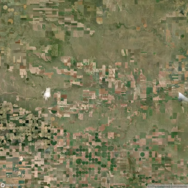 Aerial view of farmland with a patchwork of square and circular fields in various shades of green and brown.
