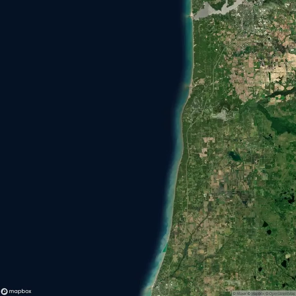Satellite image of land and shoreline along Lake Michigan, showing green vegetation, patchwork farmland, and urban areas next to a large body of dark blue water.