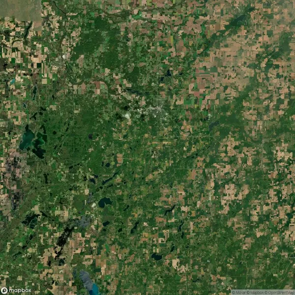 Aerial satellite view of a rural landscape featuring a patchwork of green fields, forests, lakes, and scattered small towns.