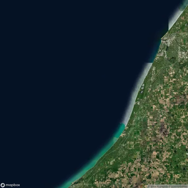 Satellite view showing a stretch of coastline with farmland and urban areas bordering a large body of dark blue water, with visible roads and grid-like agricultural plots.
