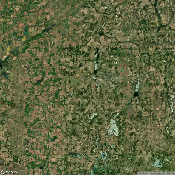 Satellite view of a patchwork landscape with fields, scattered lakes, rivers, and a small urban area near the center.