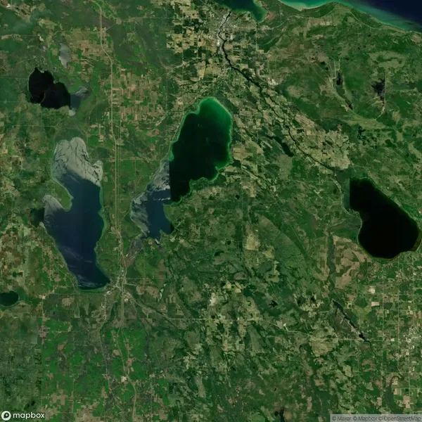 Satellite view of a green landscape with three large lakes, surrounded by patches of forest, fields, and small urban areas.