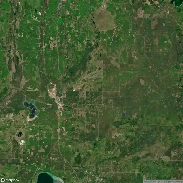 A satellite view of a rural area with scattered fields, forests, a small town, and several bodies of water. Roads and highways cross the landscape.