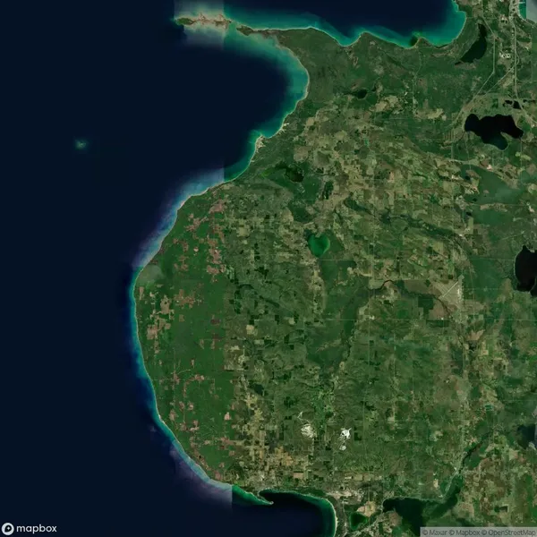 Satellite view of a large, mostly green landmass surrounded by water on three sides, featuring visible patches of farmland, forests, and scattered small settlements.