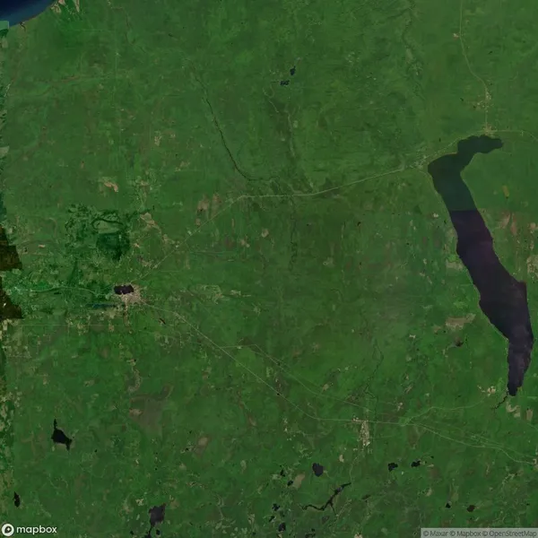 Satellite view of a green landscape with scattered lakes, a large dark body of water on the right, and a dense area near the center left, indicating possible urban development.