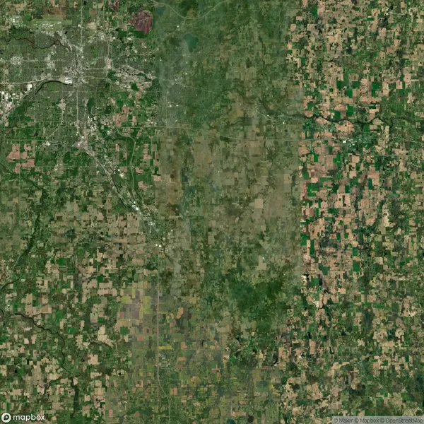 Aerial satellite view of a rural landscape with a patchwork of farmland and a densely built city area in the upper left corner.
