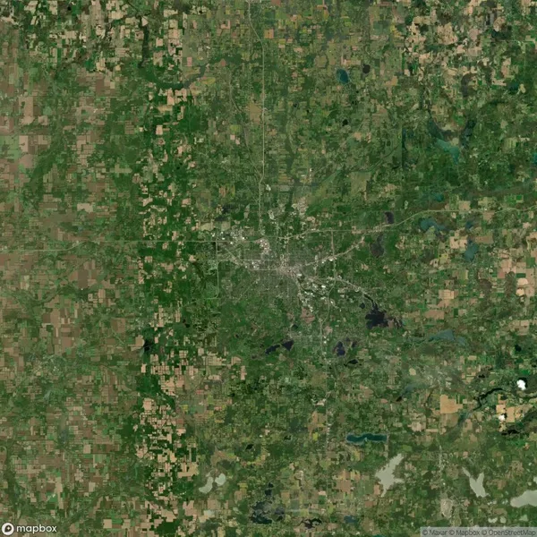 A satellite view shows a city at the center surrounded by a patchwork of green and brown farmland and wooded areas. Roads radiate outward from the city into the rural landscape.