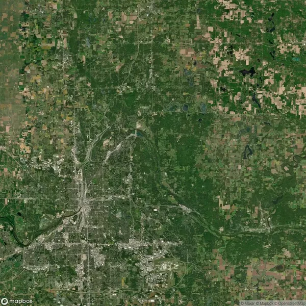 Aerial satellite image showing a city with a dense urban core, surrounded by patches of forests, farmlands, and rural areas arranged in a grid-like pattern.