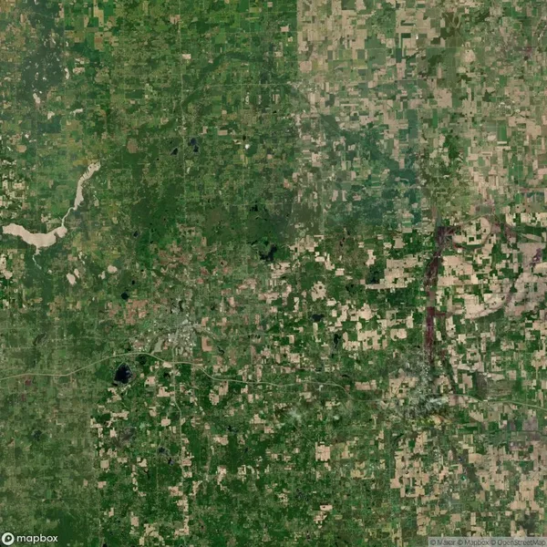 Aerial satellite view of a rural landscape with green and brown patches of farmland, roads, and scattered bodies of water.