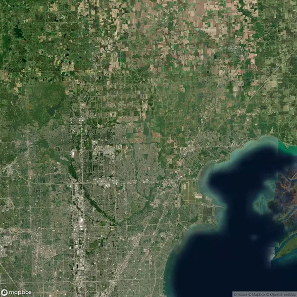 Satellite view of a sprawling urban area with dense city grids, intersecting roads, green patches, and a large body of water on the right side.