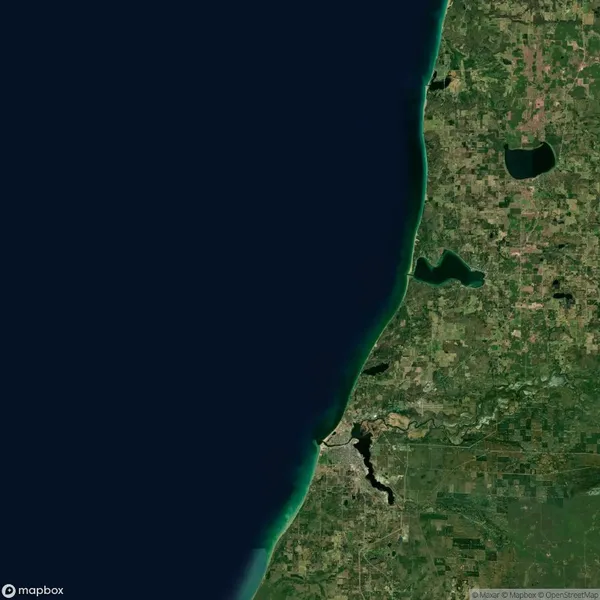 Satellite view of a coastal region showing green land, a dark body of water on the left, and patchwork fields and lakes inland on the right.