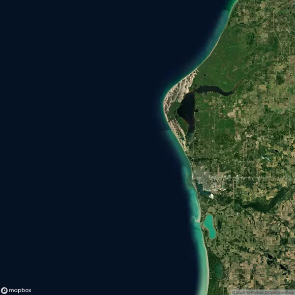 Satellite view of a coastal region with a curved shoreline, adjacent forested areas, agricultural land, and a few lakes near the bottom right.