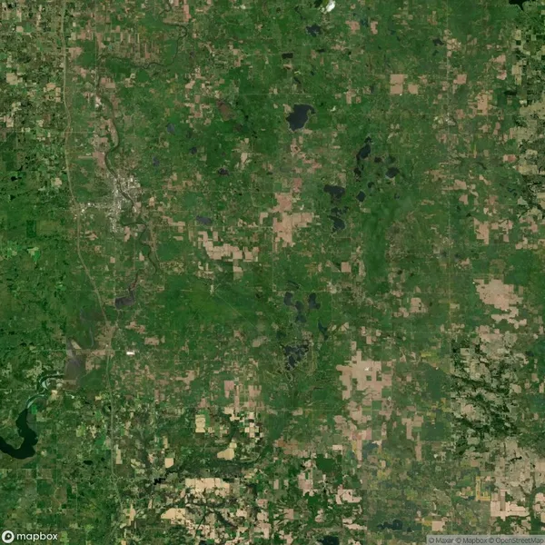 Aerial satellite view of a rural landscape featuring green fields, scattered forests, lakes, and small patches of developed or cleared land.