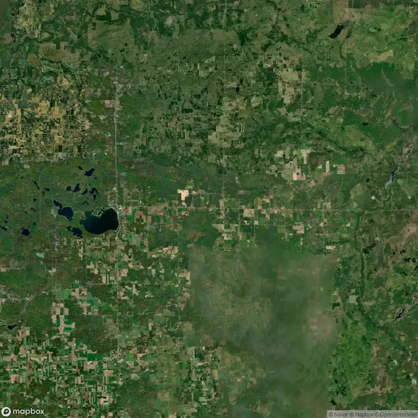 Aerial satellite view of a rural landscape with patchwork fields, green forests, and scattered lakes under a clear sky.