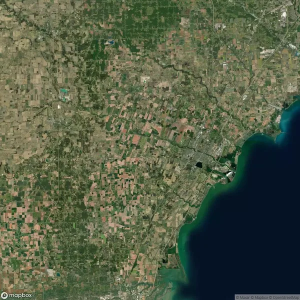 Satellite view of a region with patchwork farmland, urban areas, and a large body of water along the right side of the image.