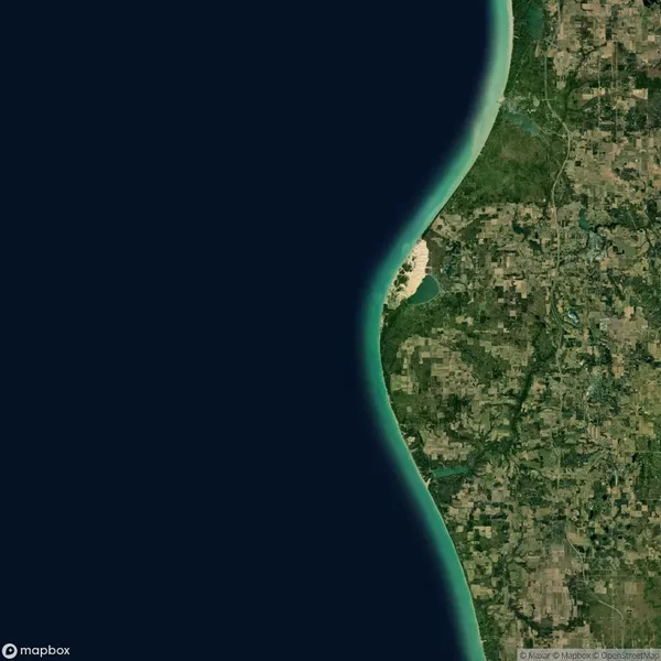 A satellite view shows a curved shoreline bordering a large body of water and a patchwork of green land with visible fields and forests inland.