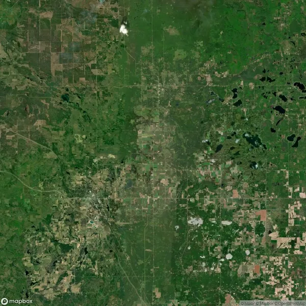 A satellite view of a rural landscape showing green fields, scattered forests, bodies of water, and a patchwork of farmland and roads.