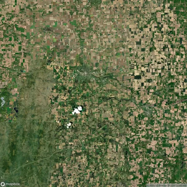 Aerial view of a patchwork landscape with agricultural fields and a few scattered clouds near the center.