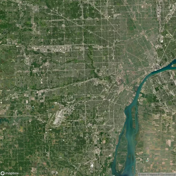 Aerial satellite view of a large urban and suburban area with a river running through the right side and a network of roads and green spaces.