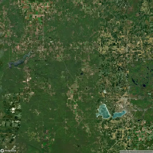 Satellite view of a rural landscape featuring fields, forests, scattered roads, and several lakes clustered near the bottom right of the image.
