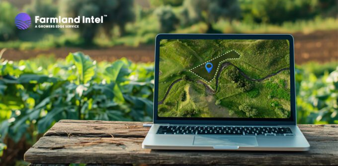 A laptop on a wooden table displays a map with a highlighted area and a pin marker, set outdoors in a farm field. Farmland Intel logo appears in the top left corner.