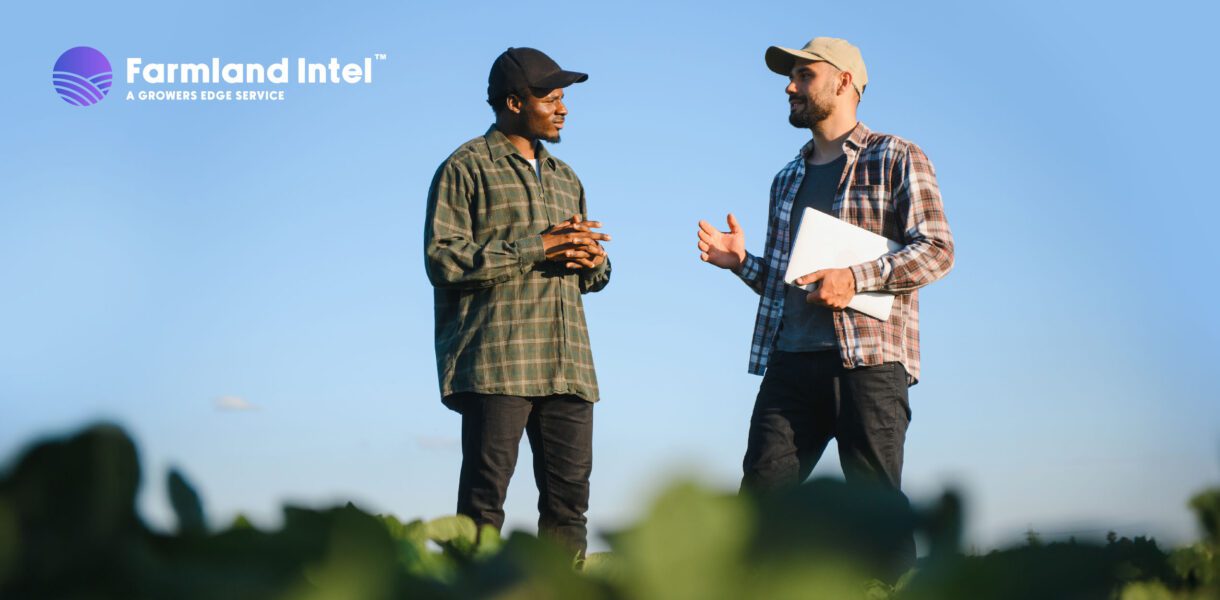 Two men in casual clothing stand in a field having a conversation; one holds a laptop. "Farmland Intel" logo appears in the top left corner.